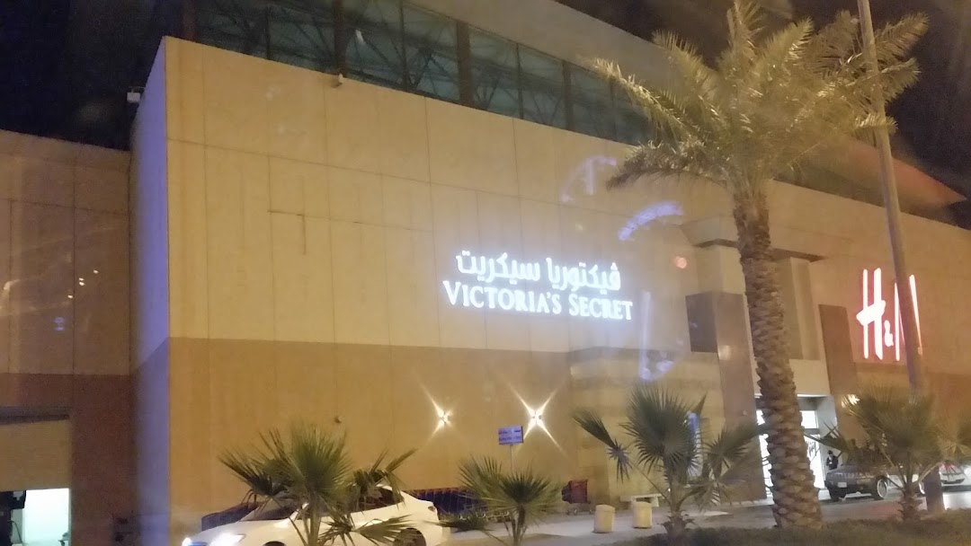 The illuminated Victoria's Secret storefront at night, with palm trees and an H&M sign visible.