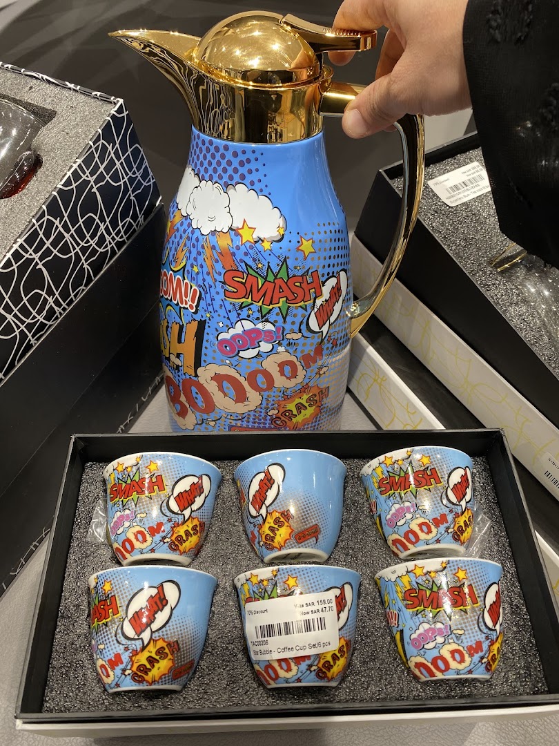 A hand holds a comic-themed thermos next to a set of matching coffee cups.
