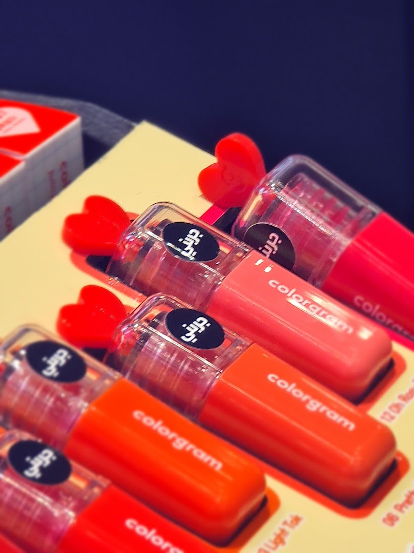 A close-up shot of several lip glosses in vibrant shades of pink and orange, with heart-shaped caps.