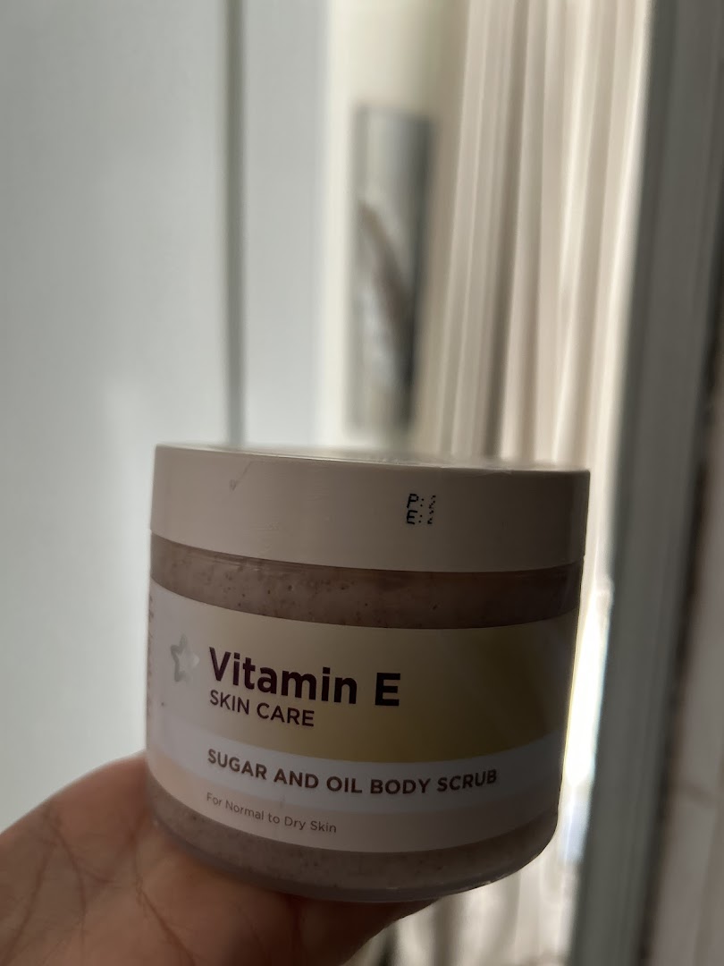 A hand holds a jar of Vitamin E Sugar and Oil Body Scrub.