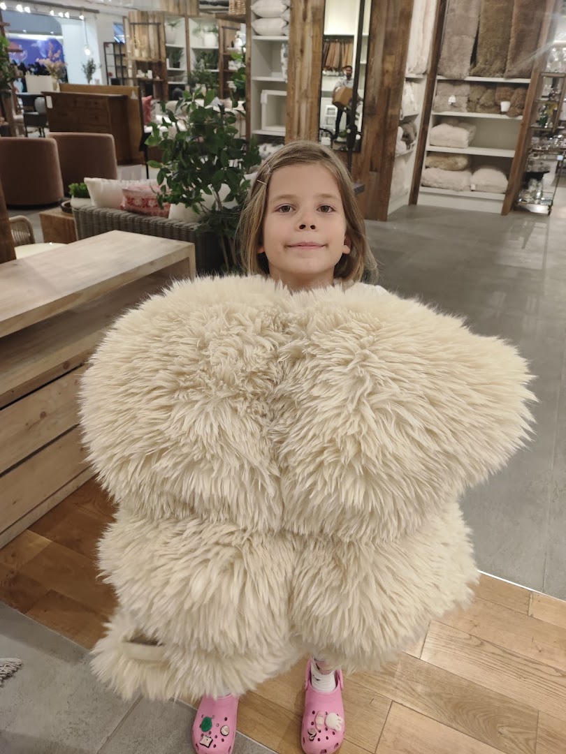 A young girl holds a fluffy cream-colored rug in a West Elm store.