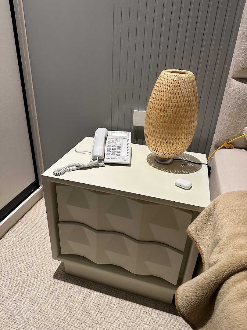 A bedside table with a lamp, phone, and blanket.