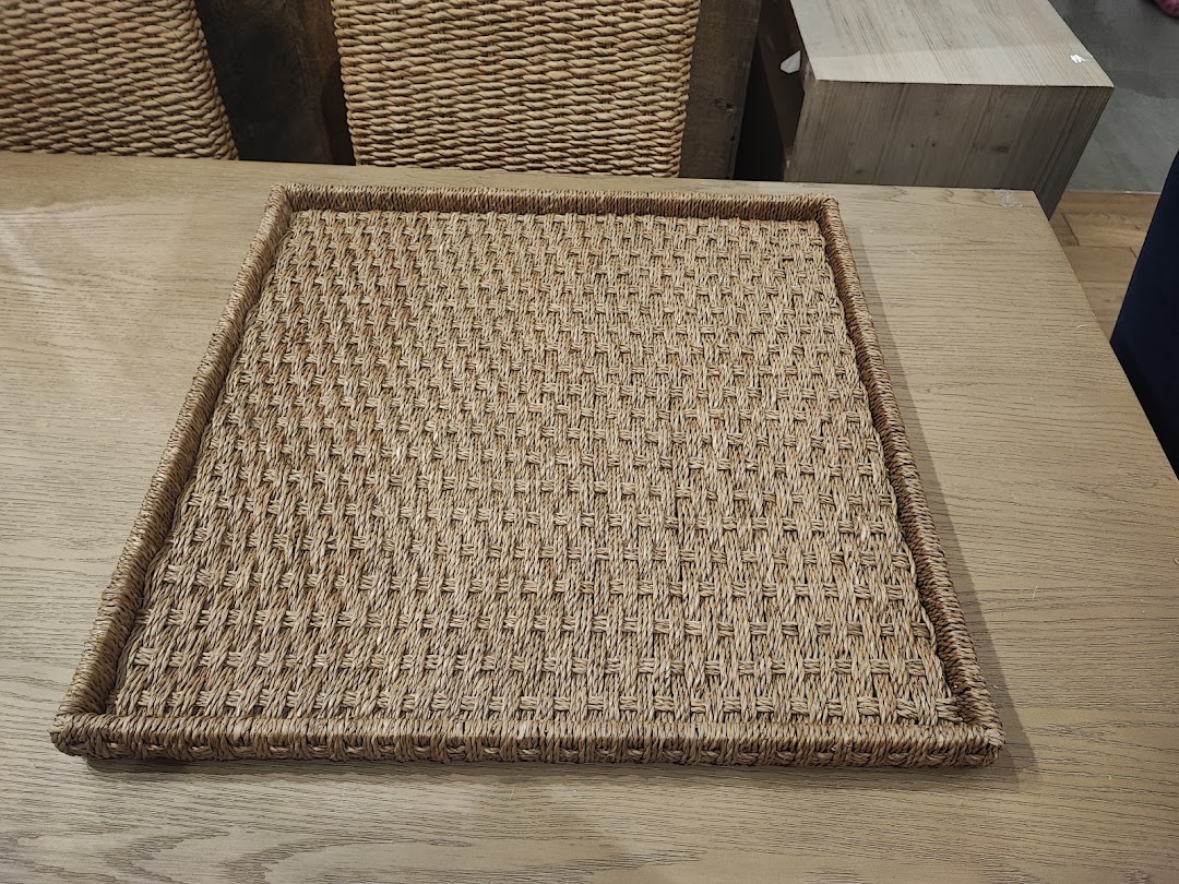 A woven tray with a textured pattern sits on a wooden table, with storage baskets in the background.