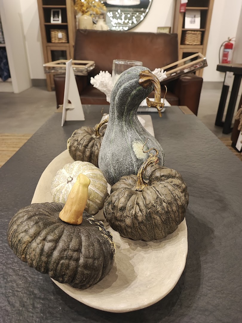 A decorative arrangement of pumpkins in a bowl on a coffee table, with furniture in the background.