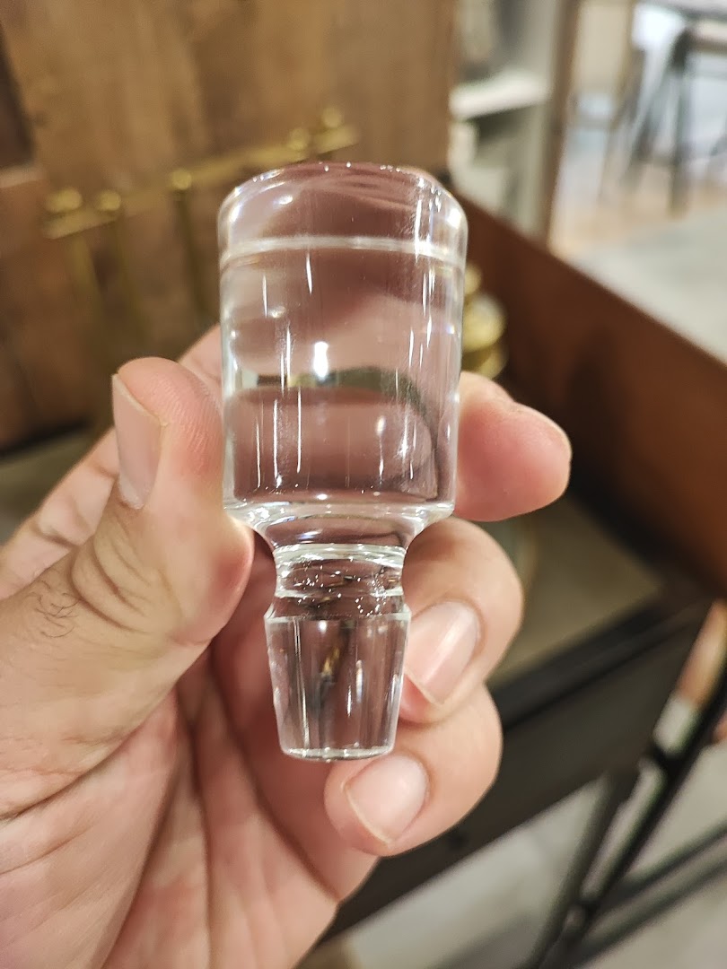 A hand holds a clear glass stopper with a faceted base.