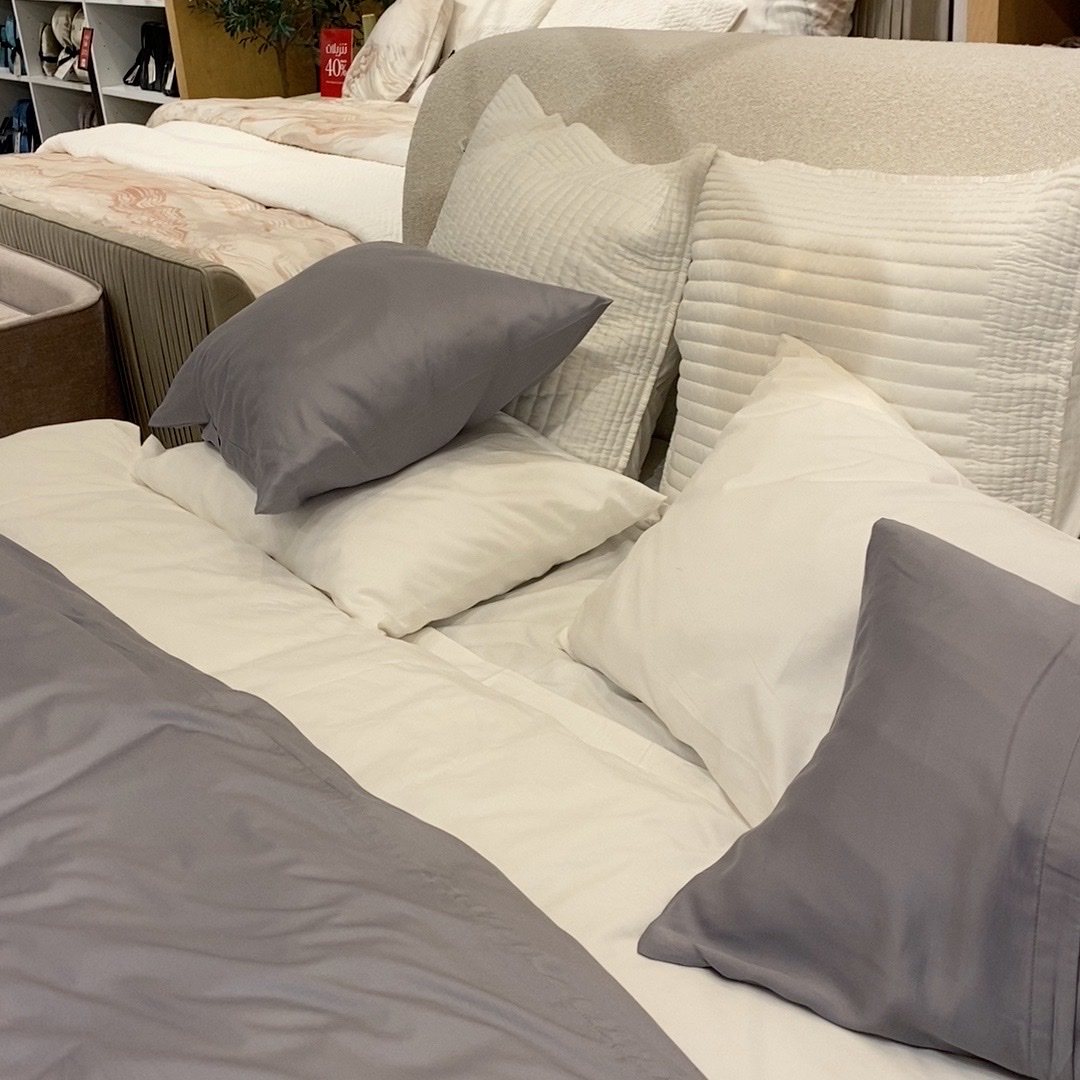 A neatly made bed with several pillows in various shades of gray and white.