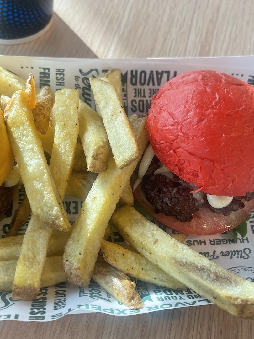 A close-up of a red-bun burger and golden fries served on branded paper.