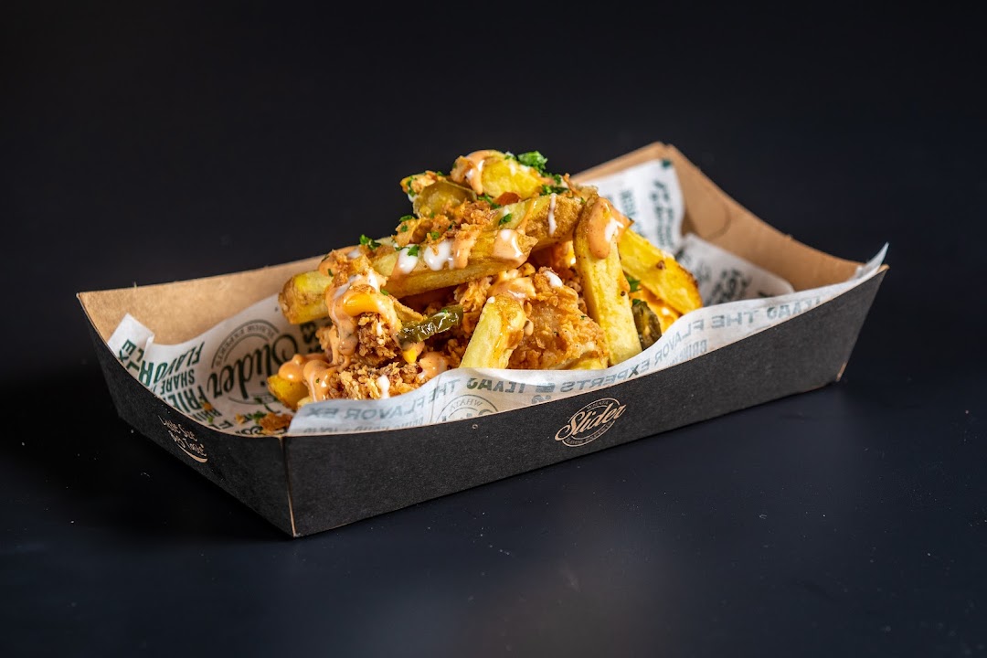 A close-up shot of loaded fries in a black cardboard container with a dark background.