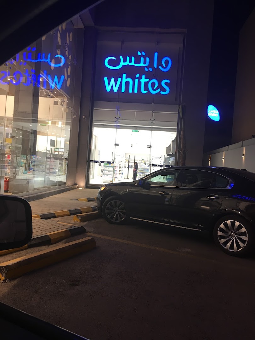 The brightly lit entrance of Whites, a modern shop, with a car parked outside.