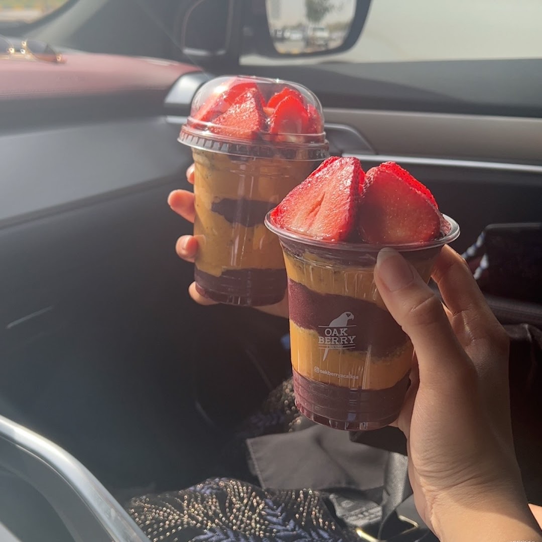 Two refreshing acai bowls with strawberries and layered fruit purees held by hands.