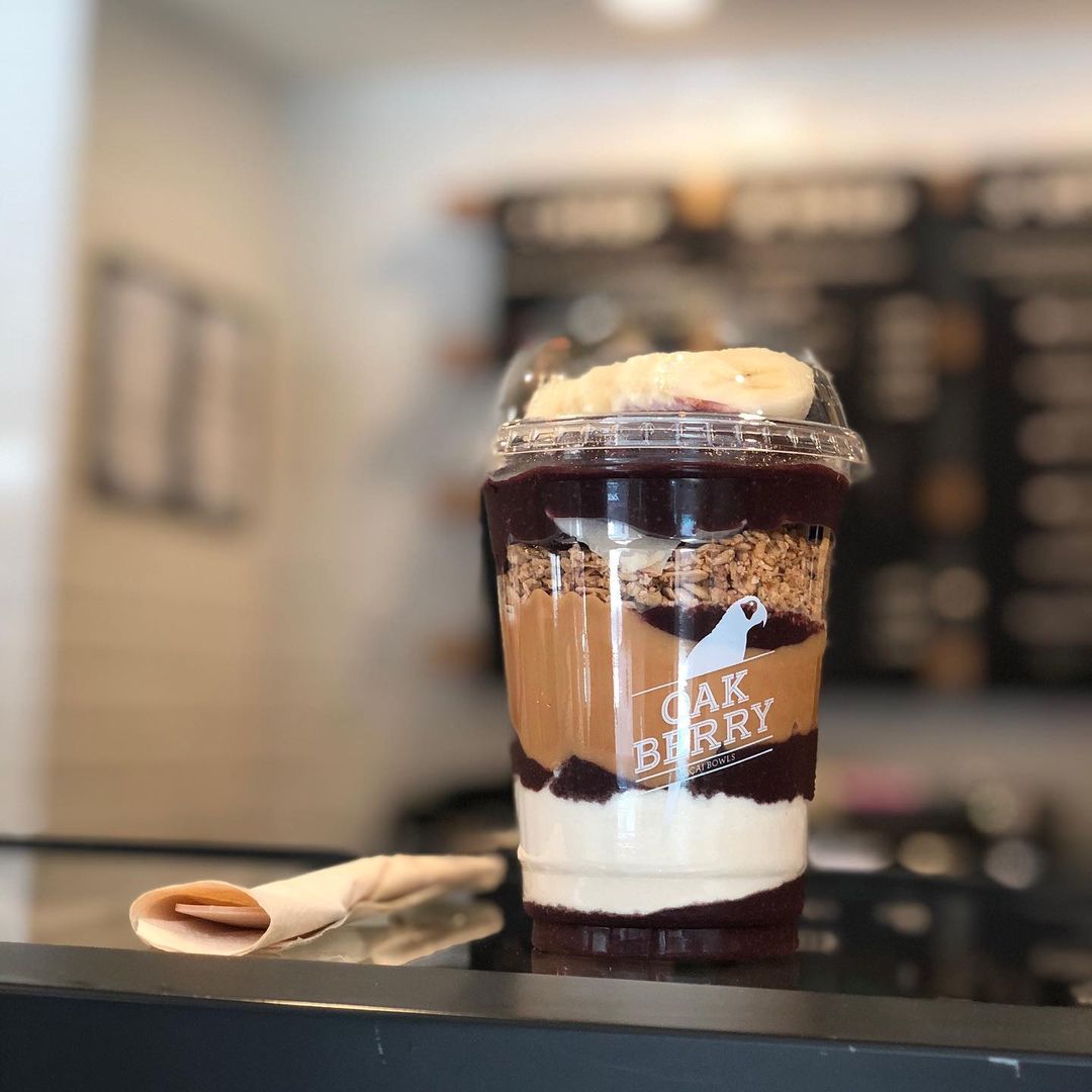 A layered acai bowl with granola, peanut butter, and banana slices in a clear cup.