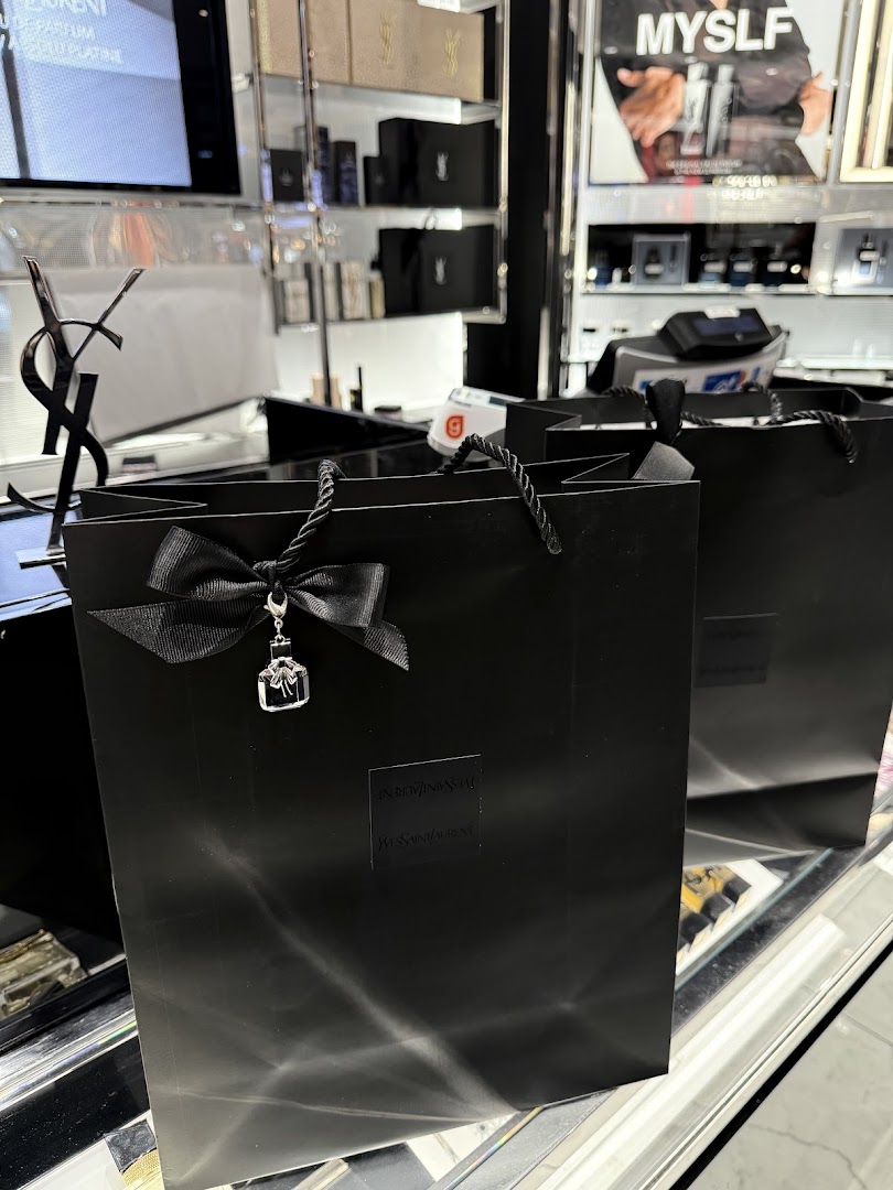Black YSL shopping bags with ribbon and charm displayed in a beauty store.
