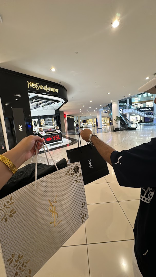 Two people holding YSL shopping bags in front of the YSL Beauty store.