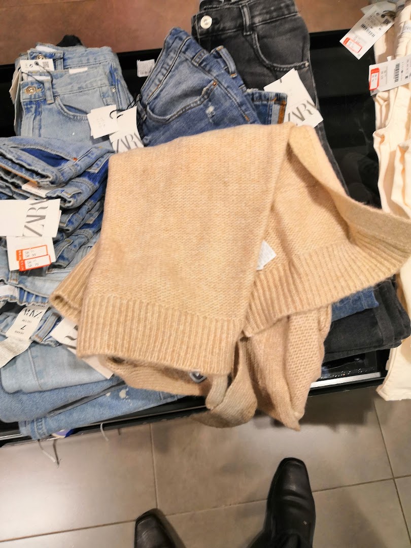 A pile of folded jeans and a beige sweater with Zara tags visible.