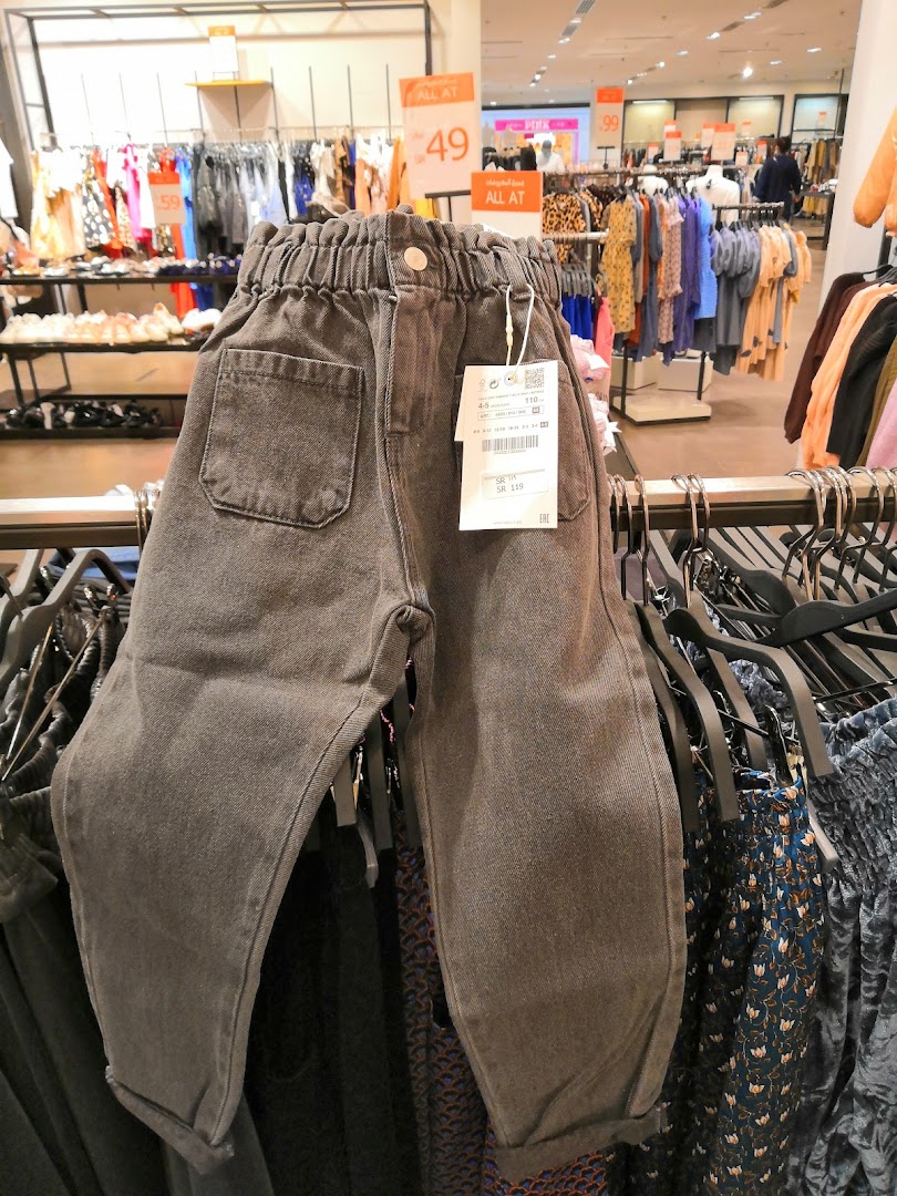 A close-up of grey children's jeans on a rack in a ZARA store, with other clothing visible.