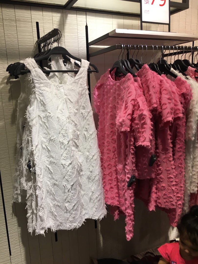 A white dress and pink tops with textured fabric displayed on hangers in a store.