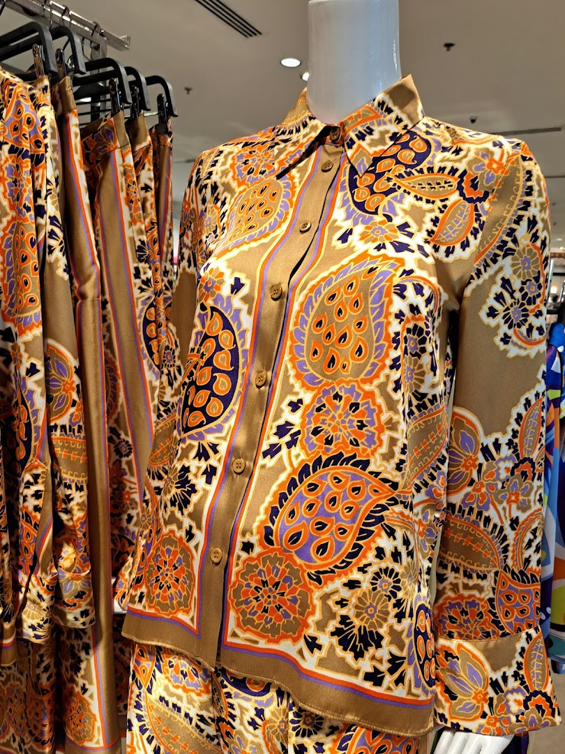 A mannequin displays a stylish brown shirt with a vibrant paisley print and matching pants.