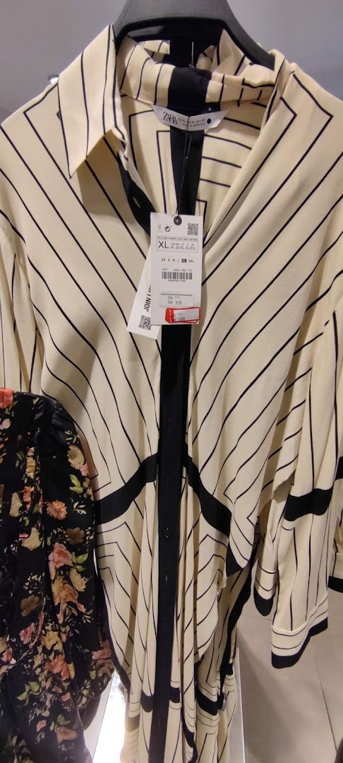 A cream-colored dress with black geometric stripes and a black floral dress are displayed on hangers.