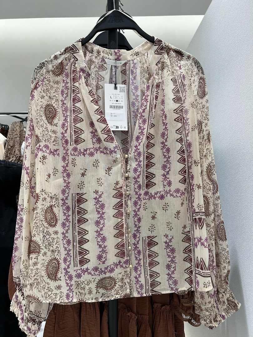 A patterned blouse with a V-neck and buttons, displayed on a hanger.