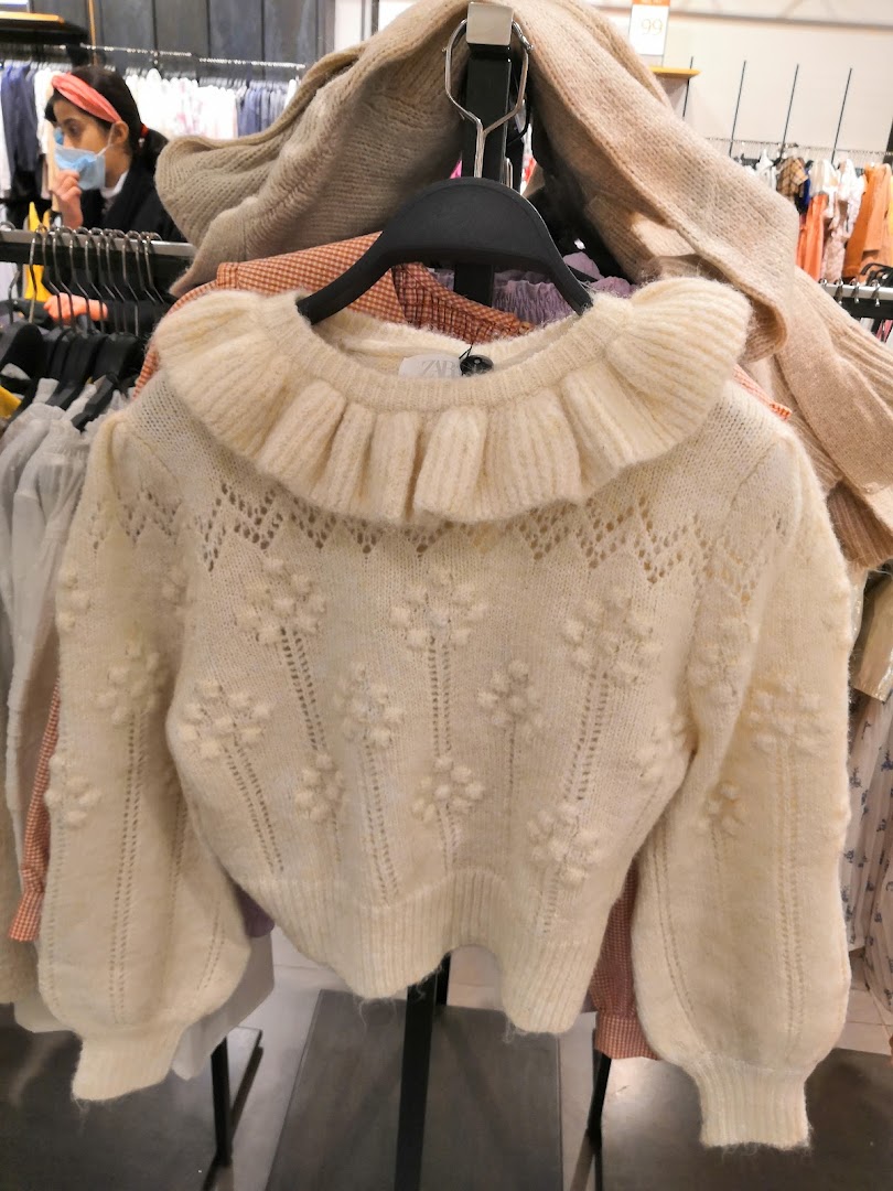 A cream-colored sweater with a ruffled collar and floral pattern is displayed.