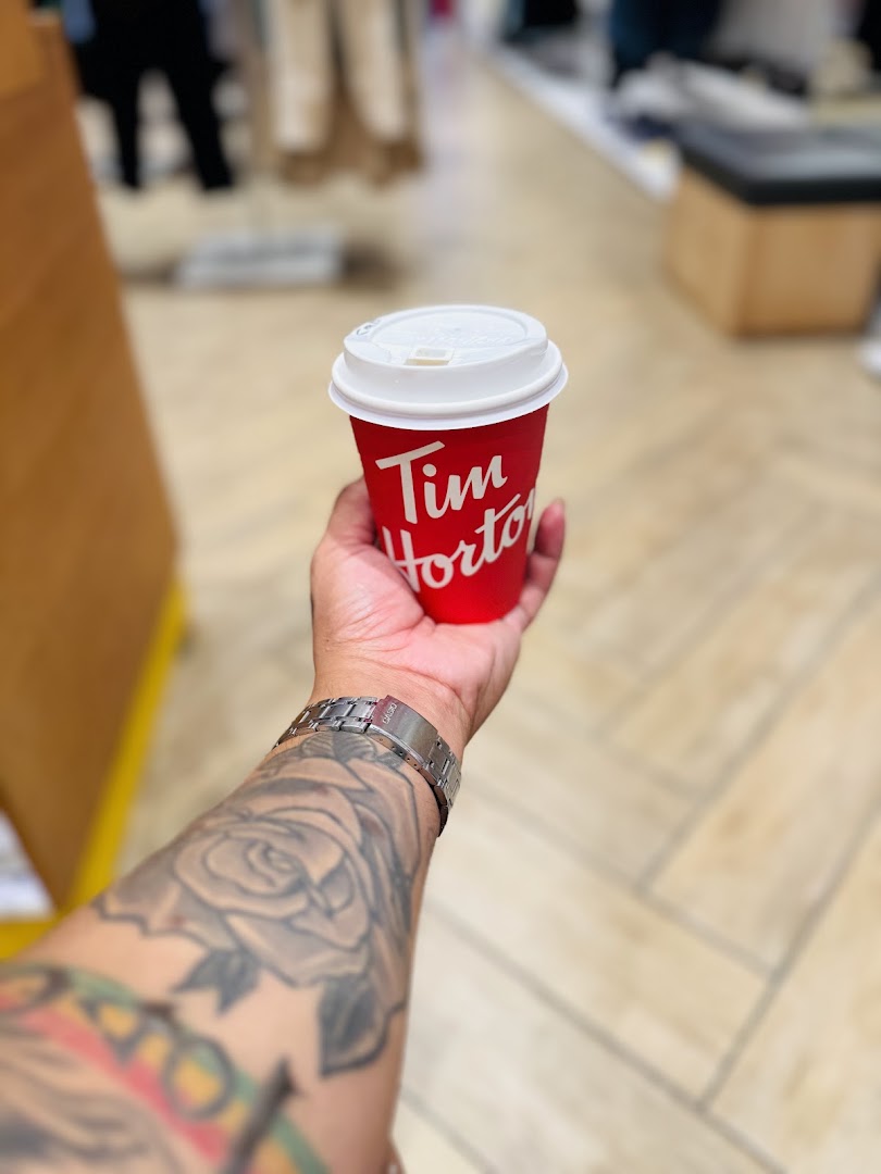 A hand holds a red Tim Hortons coffee cup with a white lid.